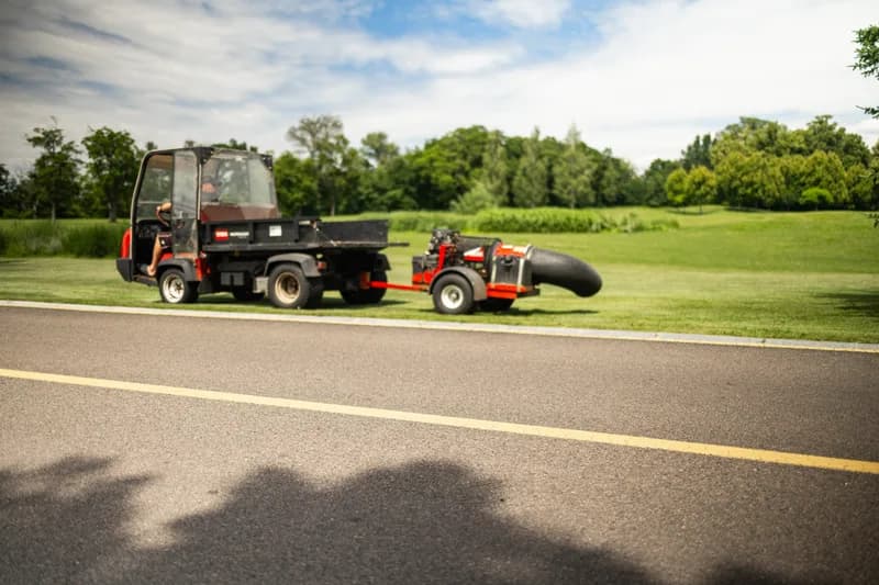 Operator driving commercial landscaping utility vehicle with trailer equipment