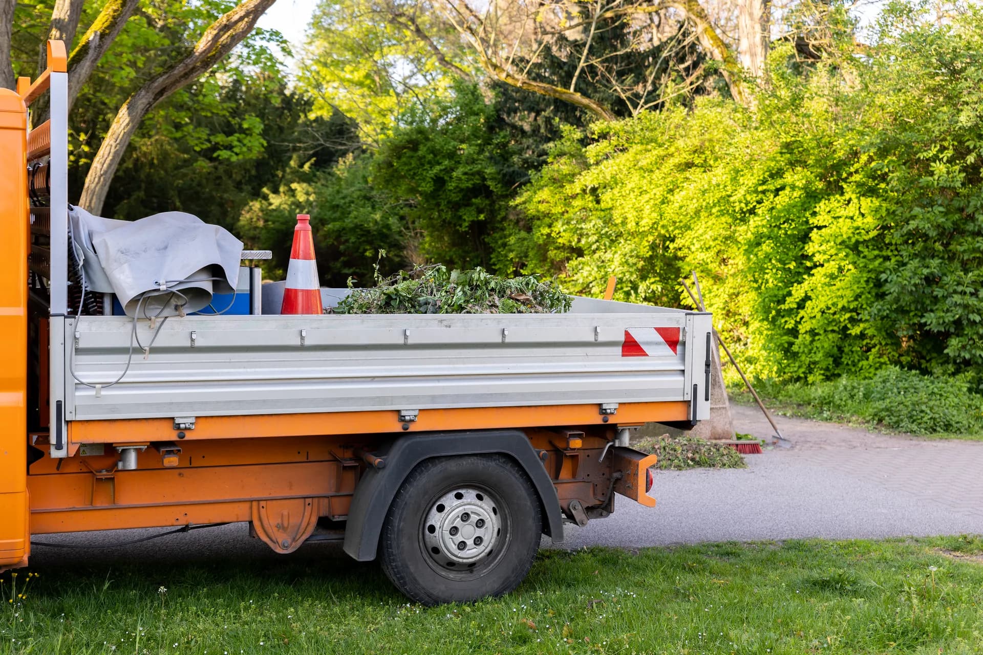 Orange landscape work truck loaded with yard vegetation beside a paved path